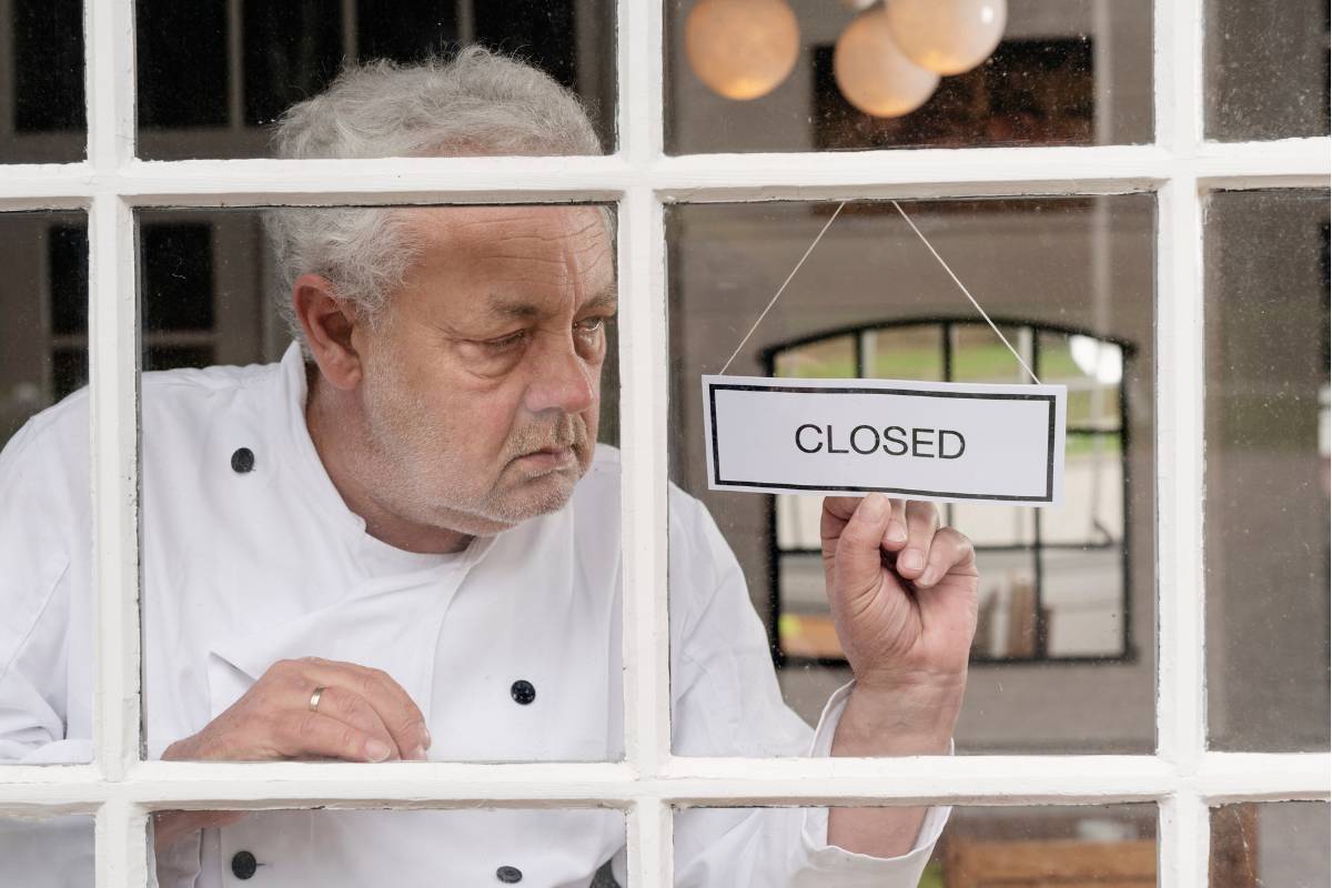 Chef de cozinha colocando uma placa de "fechado" na janela de um restaurante, com expressão preocupada