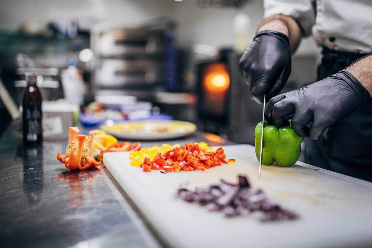 Chef cortando pimentão verde em uma cozinha profissional, representando o Mise en Place na cozinha