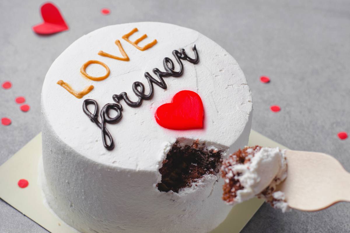 Bentô Cake branco com a frase 'Love forever' e um coração vermelho, com uma fatia retirada, mostrando o interior do bolo.