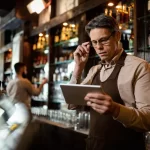Dono de bar consultando tablet no balcão para avaliar sistema de gestão para bares