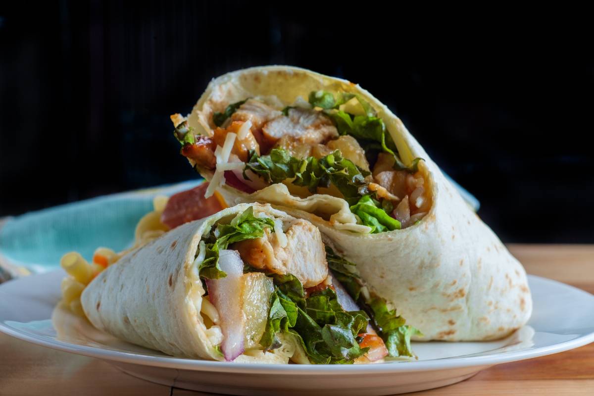 Wrap recheado com frango, alface e queijo, servido em prato branco