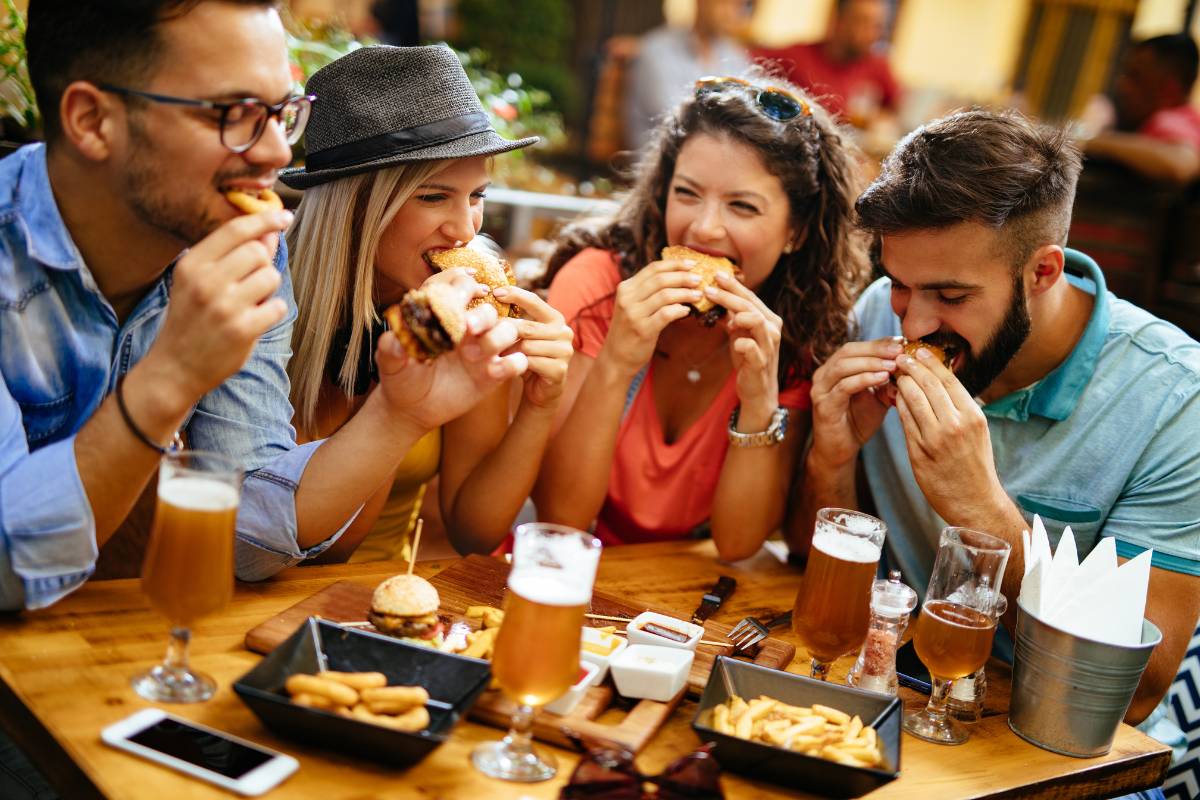 Grupo de amigos se divertindo em um restaurante, comendo hambúrgueres e batatas fritas em um ambiente descontraído