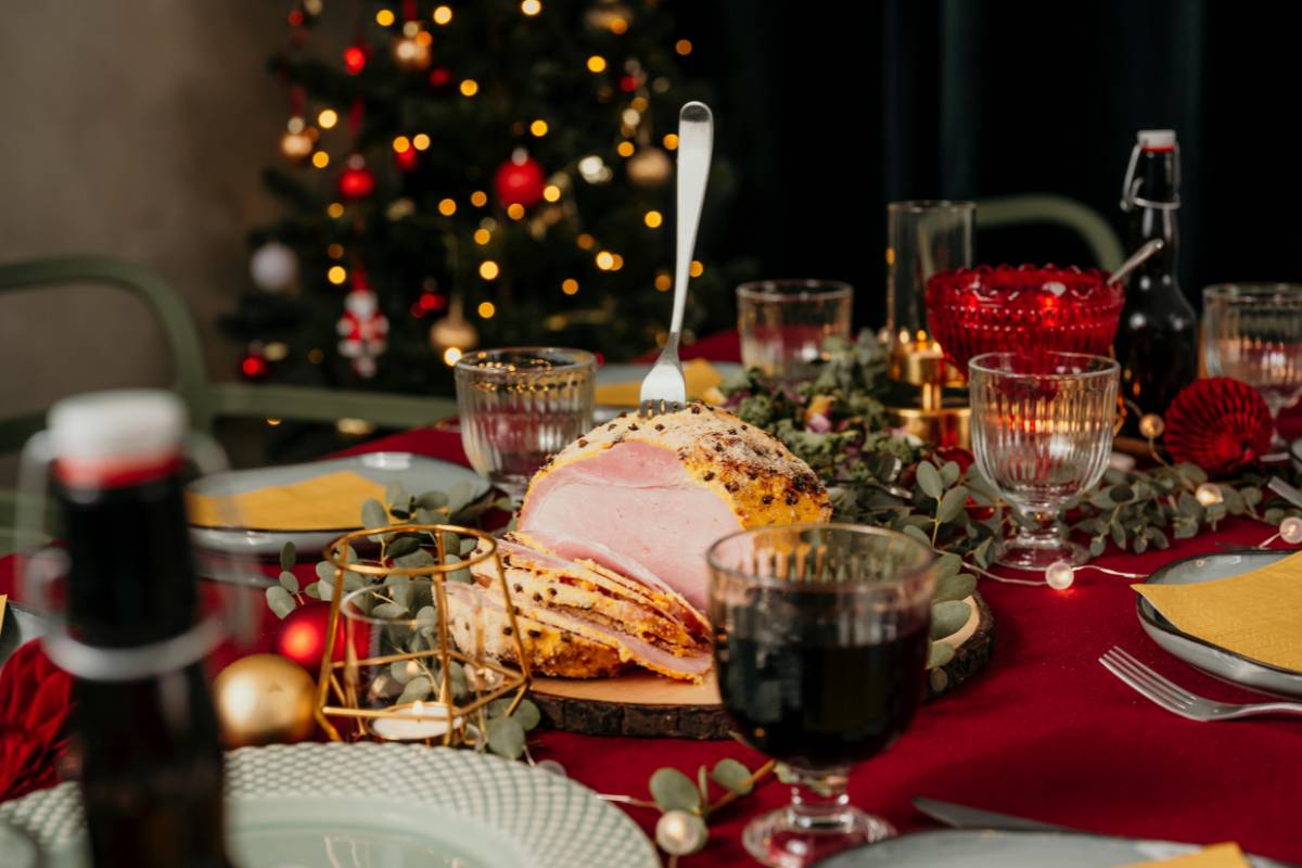 Mesa posta para a ceia de Natal, com tender decorado com cravos e iluminação festiva ao fundo.