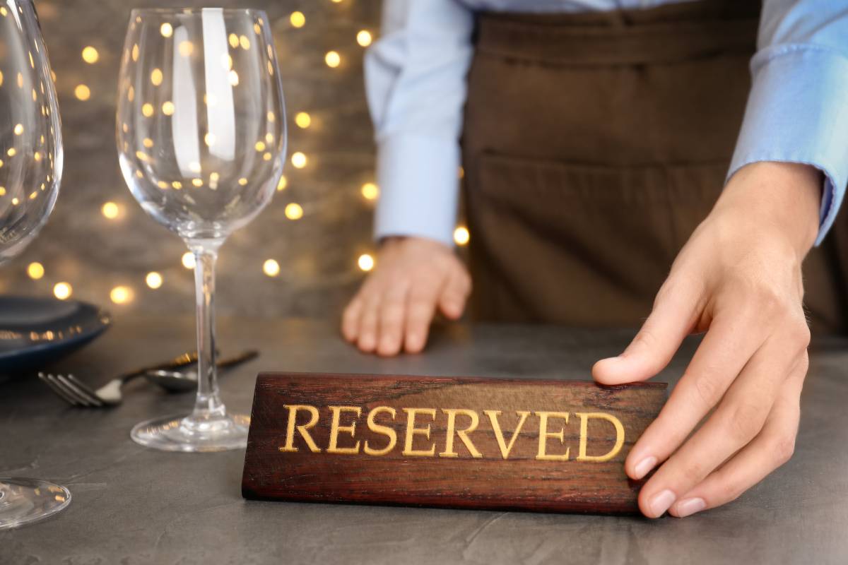 Garçom colocando uma placa de “Reservado” em uma mesa arrumada em um ambiente de restaurante.