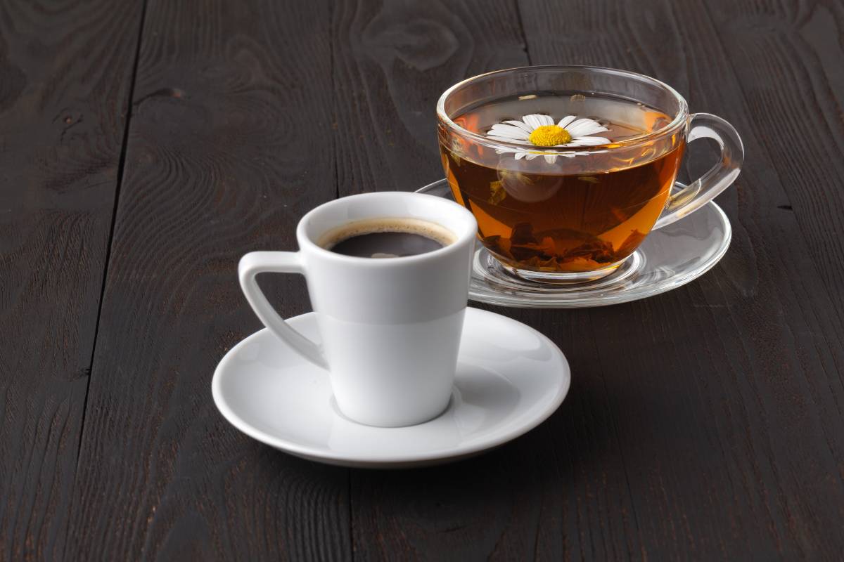 Café e chá de camomila: Xícara de café preto e chá de camomila servido em uma xícara de vidro transparente, sobre uma mesa de madeira escura.