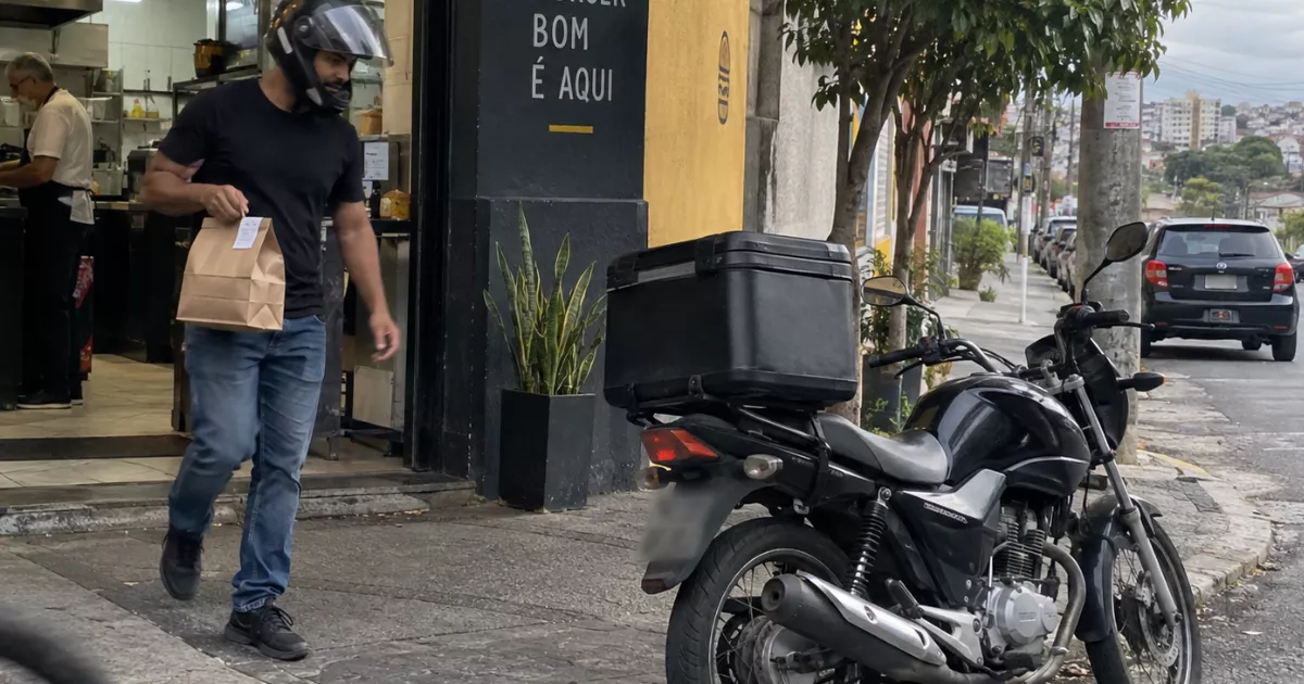 Entregador sai de uma hamburgueria com o pedido e caminha em direção à motocicleta.