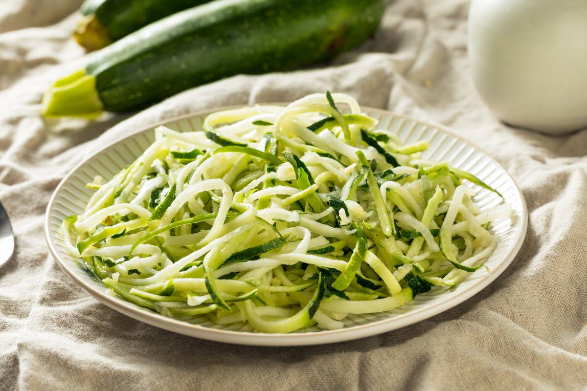 Macarrão de abobrinha low carb: Prato com espaguete de abobrinha, fresco e crocante, servido em um prato branco rústico com fundo de tecido bege.