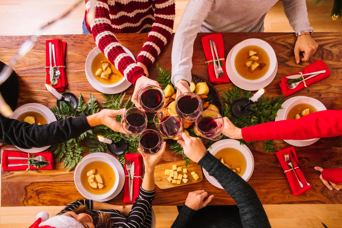 Grupo de pessoas fazendo um brinde com vinho ao redor de mesa posta com pratos típicos de ceia de Natal, decoração festiva e clima de confraternização em restaurante