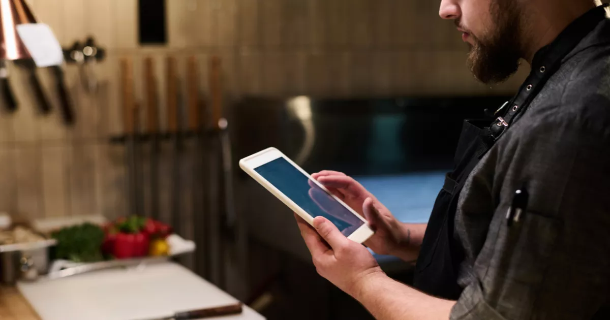 Profissional de cozinha usando tablet para acompanhar pedidos em um sistema PDV para delivery dentro do restaurante.