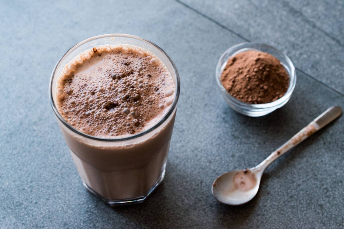 Smoothie de chocolate low carb: Smoothie cremoso de chocolate, servido em copo transparente com pó de cacau ao lado.