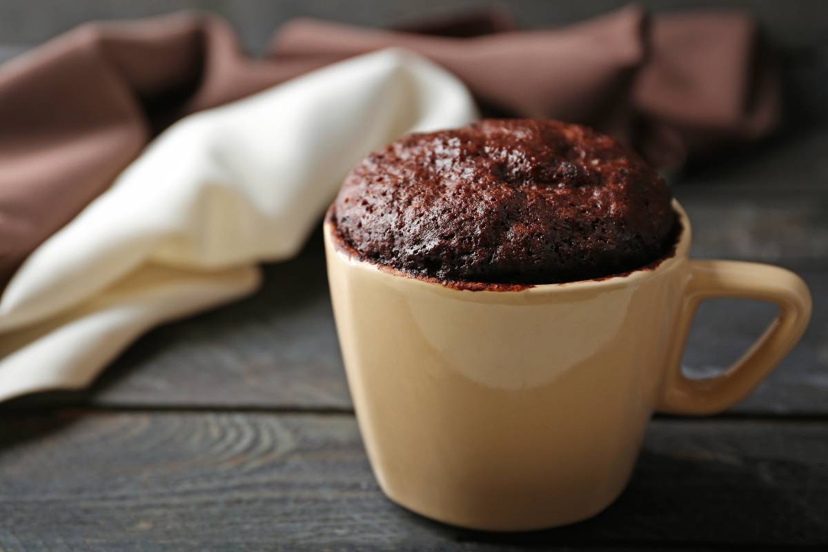 Bolo de caneca low carb de chocolate: Bolo de chocolate low carb servido em uma caneca bege, com textura úmida e aparência apetitosamente caseira.