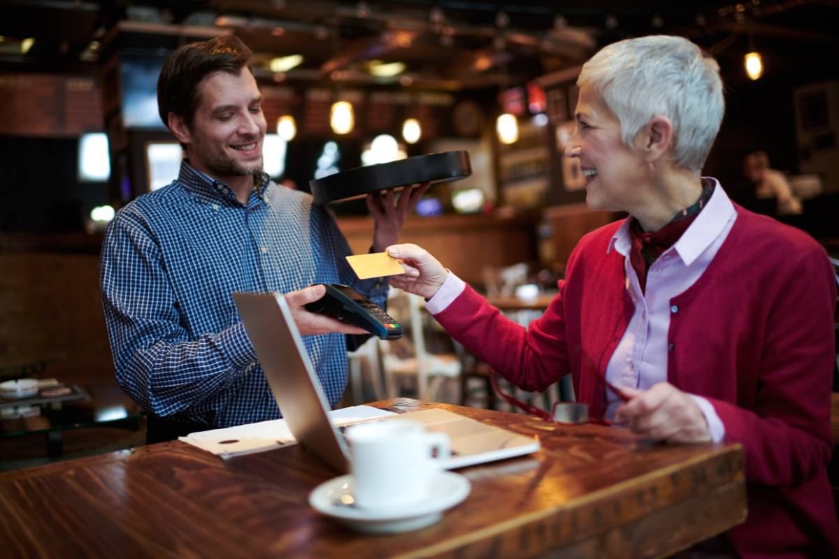 Funcionário de um restaurante sorrindo enquanto processa o pagamento com cartão em uma máquina, ilustrando a praticidade e flexibilidade de aceitar diversas formas de pagamento, incluindo tickets alimentação e refeição.
