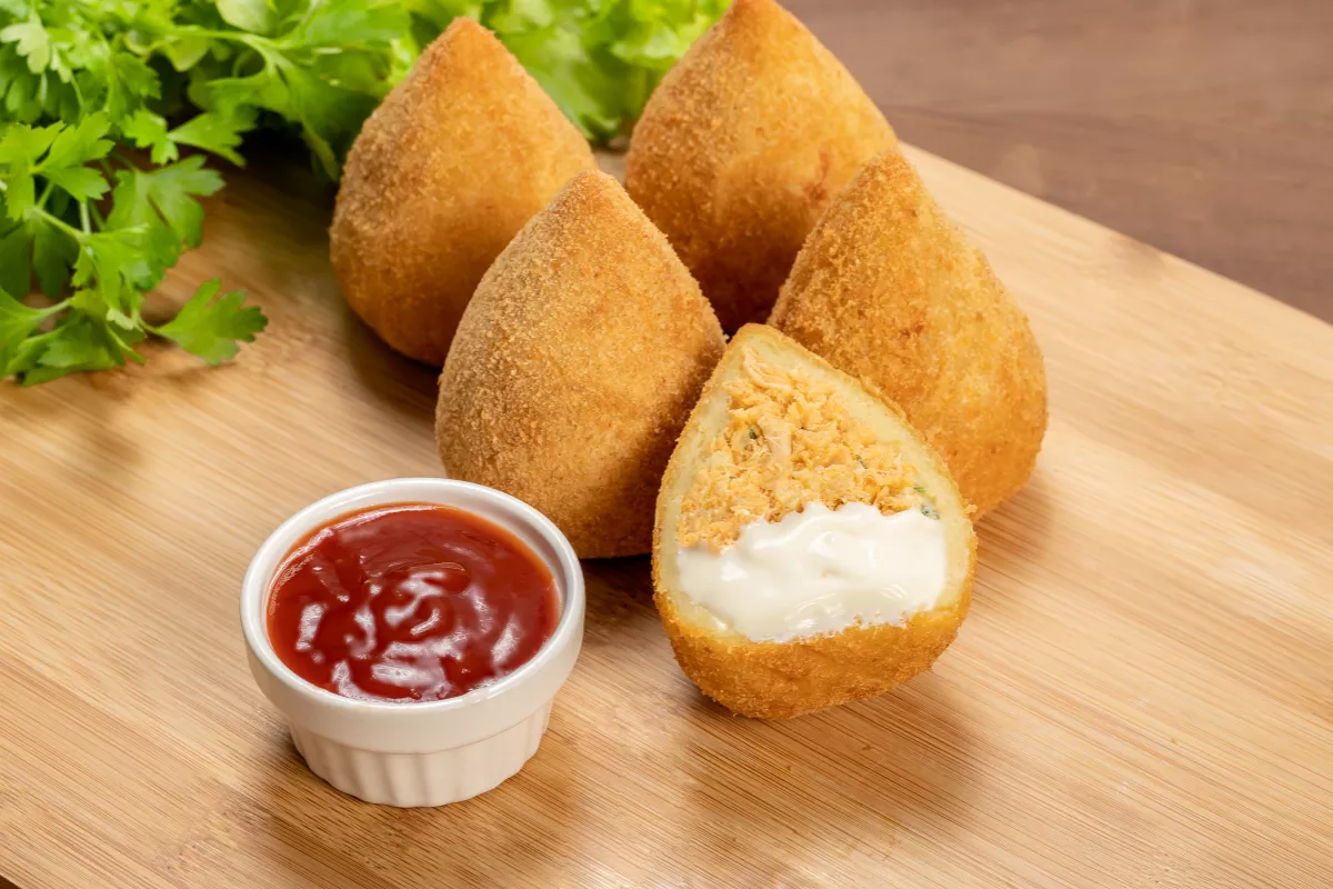 Coxinha de frango com catupiry: Salgado brasileiro clássico recheado com frango desfiado e queijo cremoso tipo catupiry, acompanhado de molho de tomate.