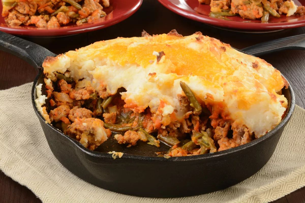 Escondidinho de carne com queijo gratinado: Um prato tradicional servido em panela de ferro, com purê cremoso de batatas, carne moída temperada e cobertura de queijo derretido.