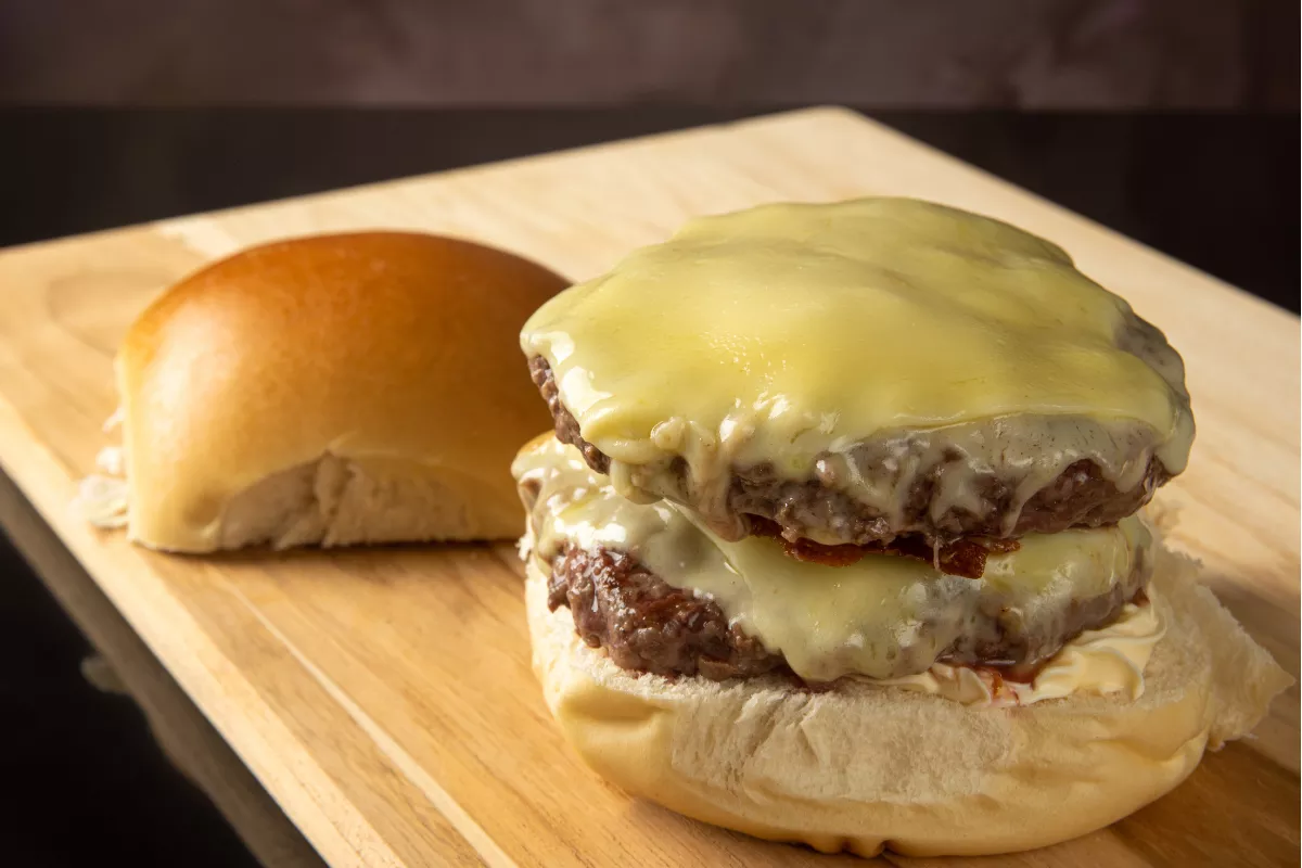 Hambúrguer com queijo duplo: Um delicioso hambúrguer artesanal com dois suculentos discos de carne, queijo derretido e pão macio, montado em uma apresentação gourmet.