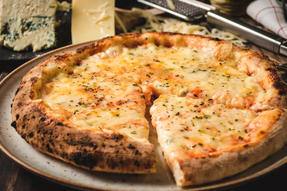 Pizza quatro queijos artesanal: Pizza assada em forno rústico, coberta com uma mistura de queijos como parmesão, gorgonzola, mozzarella e brie.