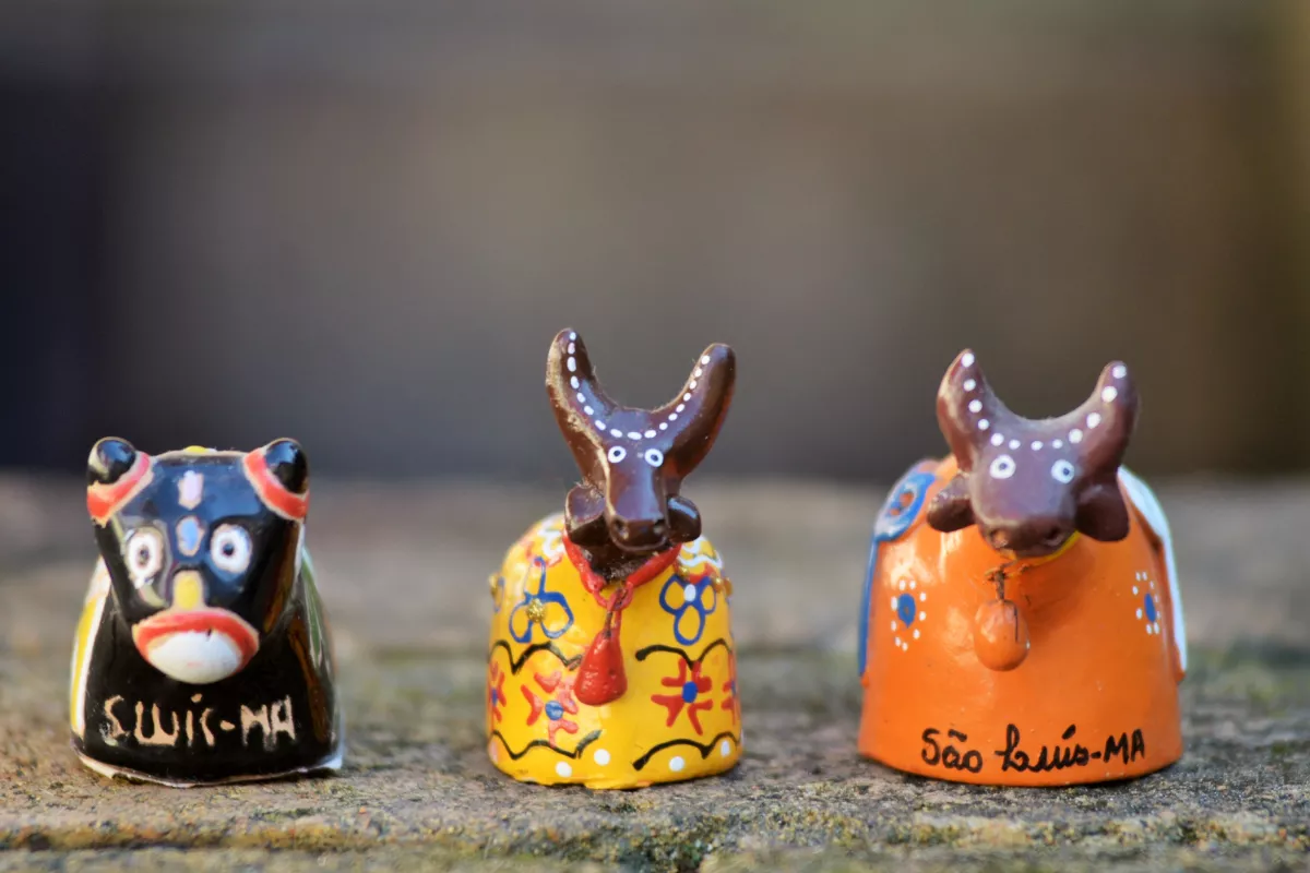 Três miniaturas artesanais coloridas do Bumba Meu Boi com inscrições de São Luís-MA, posicionadas sobre uma superfície de pedra. Representam a cultura popular nordestina e sua riqueza como inspiração para decorações e cardápios temáticos.

