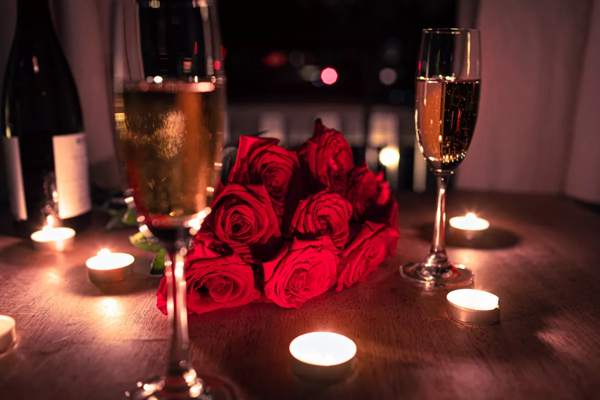 Mesa decorada para jantar romântico, com taças de espumante, buquê de rosas vermelhas e velas acesas, criando um clima intimista ideal para promoção de Dia dos Namorados em restaurante.