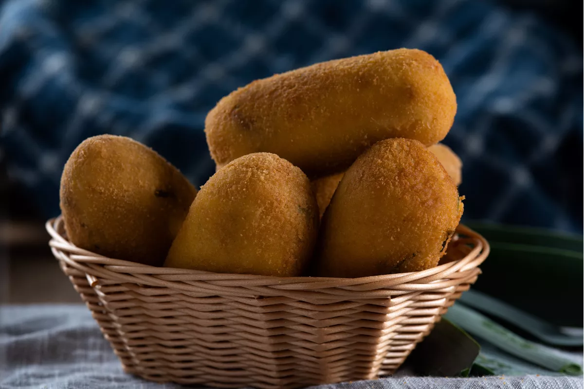 Cesta de bolinhos de mandioca empanados e fritos, com casquinha dourada, ideais como entrada afetiva e prática para o Dia das Mães.