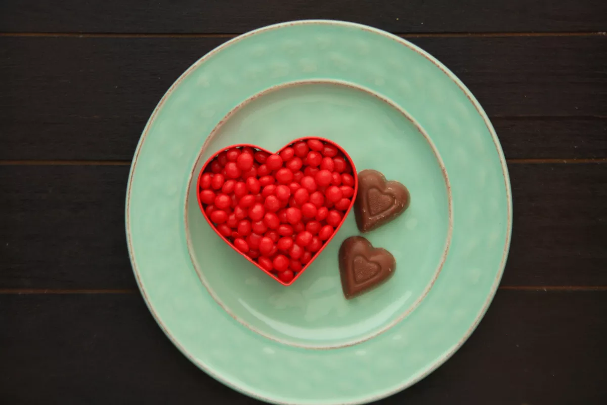 Prato verde com bombons de chocolate em formato de coração e confeitos vermelhos, sugerindo uma sobremesa criativa e temática para ações promocionais de restaurante no Dia dos Namorados.