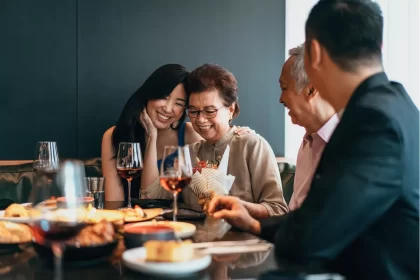 Família asiática reunida em restaurante, brindando com taças de vinho e sorrindo ao redor da mesa, representando o clima afetivo e acolhedor da data comemorativa.