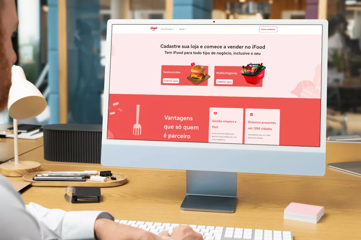 Pessoa utilizando um computador para acessar a página de cadastro de lojas no site do iFood, que exibe opções para restaurantes e multicategorias, destacando vantagens como gestão simples e presença em mais de 1.200 cidades, reforçando o processo de como criar uma loja no iFood.