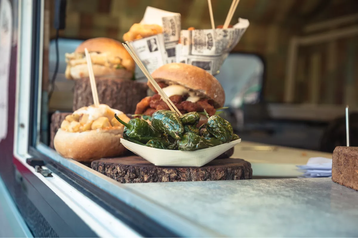 Detalhe de balcão de food truck com hambúrgueres artesanais, batatas fritas e pimentões assados, mostrando a variedade de alimentos servidos.


