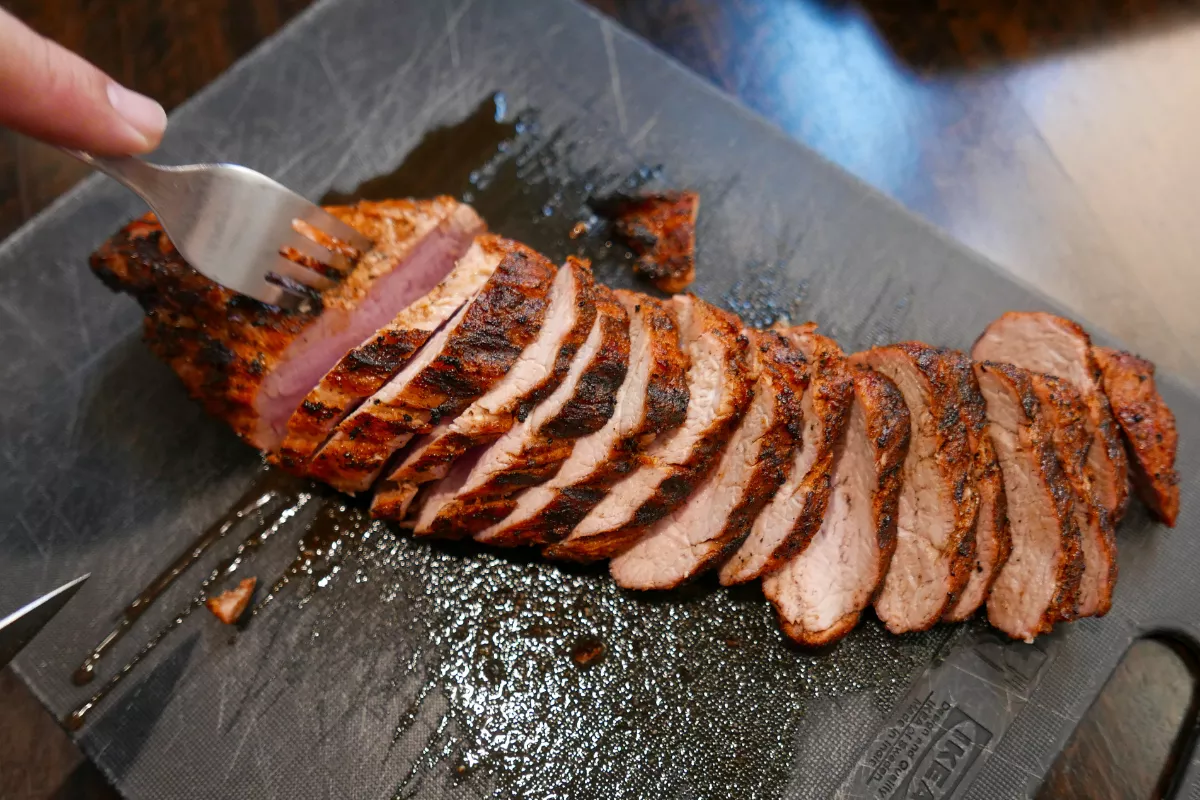Filé mignon suíno grelhado em fatias, com crosta dourada e interior suculento, servido sobre tábua, perfeito para compor menus sofisticados e de alta margem.