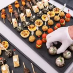 Bandejas organizadas com diferentes tipos de finger foods, como mini quiches, espetinhos e canapés, prontas para servir em eventos e coquetéis.