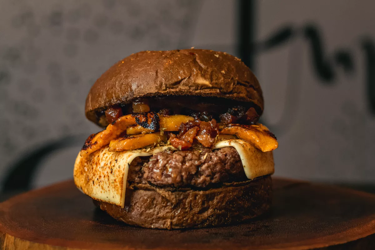 Hambúrguer artesanal com pão escuro, carne grelhada, queijo derretido e vegetais assados, montado com apresentação rústica. Feito à mão com ingredientes frescos.