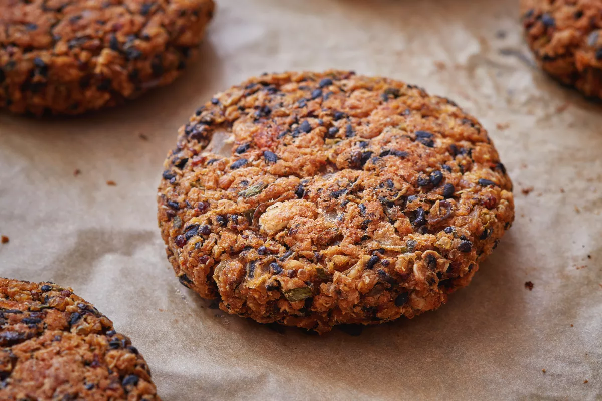 Hambúrguer vegano feito à base de grãos e vegetais, com textura crocante e aparência rústica. Opção saudável e sem ingredientes de origem animal.