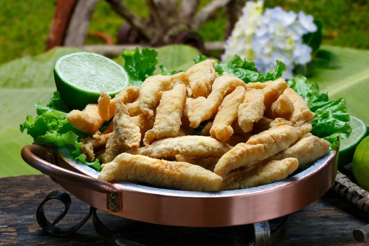 Iscas de peixe empanadas no fubá, fritas até dourar e servidas em recipiente de cobre com folhas verdes e limão, ótima opção de entrada crocante para almoços afetivos.