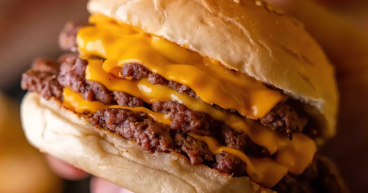 Cheeseburger triplo em close, com discos finos de carne intercalados por cheddar derretido em pão macio, o tipo de hambúrguer que mais cresce no Brasil