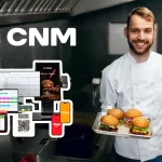 Chef de hamburgueria sorrindo e segurando uma bandeja com hambúrgueres artesanais na cozinha, ao lado de recursos do sistema CNM, como PDV, cardápio digital, delivery e integrações com maquininhas. Representa a modernização da gestão em hamburguerias com o CNM.