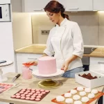 Empreendedora confeiteira finalizando decoração de bolo com topo personalizado, simbolizando a importância da gestão e cuidado nos detalhes desde o início do negócio.