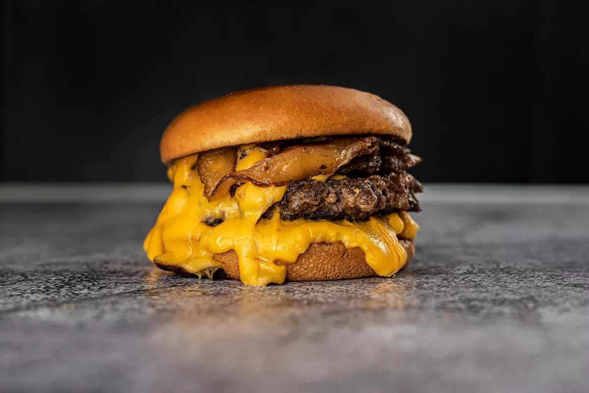 Smash burger com carne prensada, queijo derretido em abundância e pão macio, sobre superfície escura. Ideal para quem busca crocância e suculência.