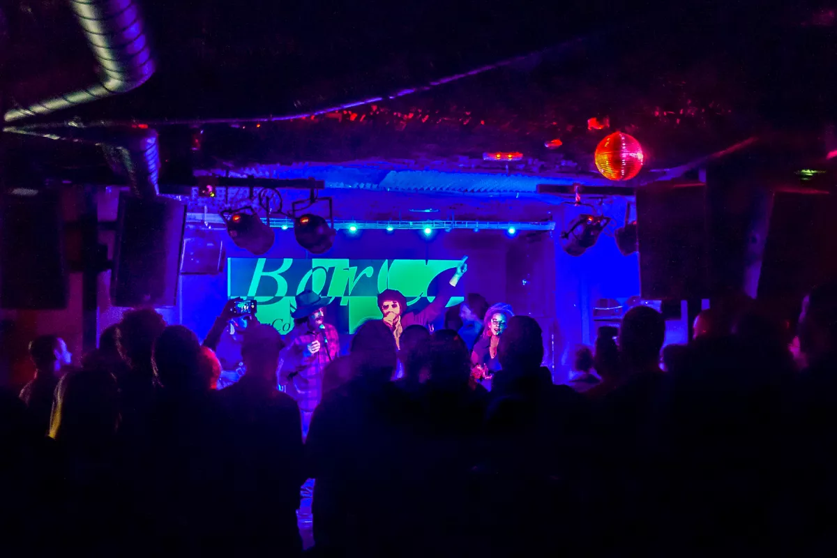 Público curtindo show ao vivo em bar com palco iluminado em azul e banda se apresentando, representando eventos temáticos no Dia Mundial do Rock.