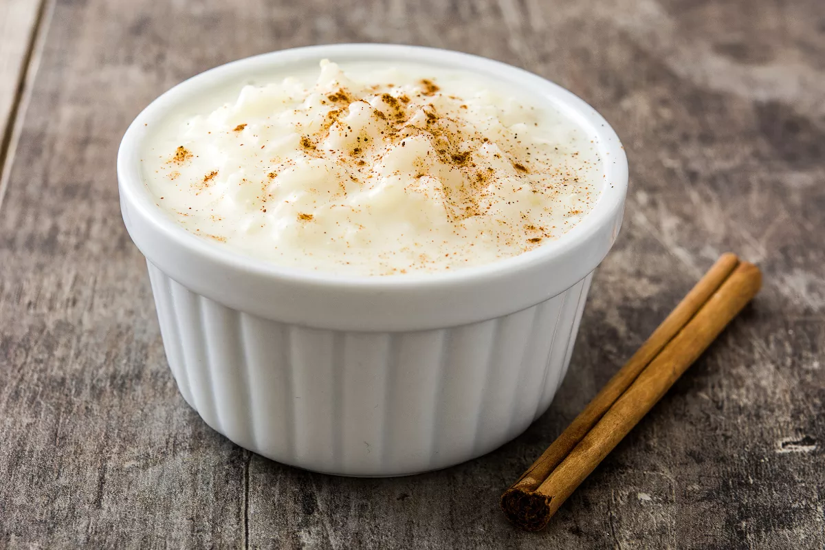 Tigela de arroz doce cremoso polvilhado com canela, decorada com pau de canela, em ambiente rústico típico das festas juninas.