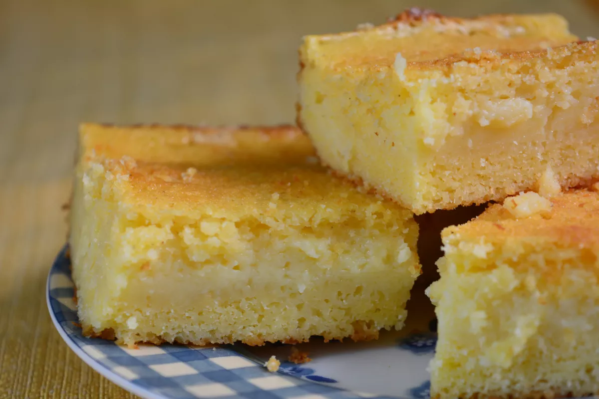 Fatias de bolo de fubá úmido e dourado, com pedaços de goiabada derretida, servidos em prato xadrez, aroma que conquista na festa junina.