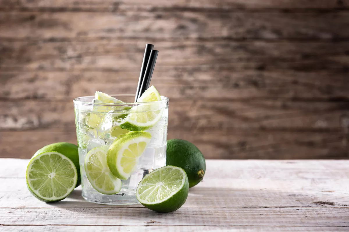 Copinho baixo com caipiroska de limão servido com gelo e rodelas da fruta, sobre mesa rústica de madeira. Uma bebida refrescante e simples, ideal para qualquer bar.