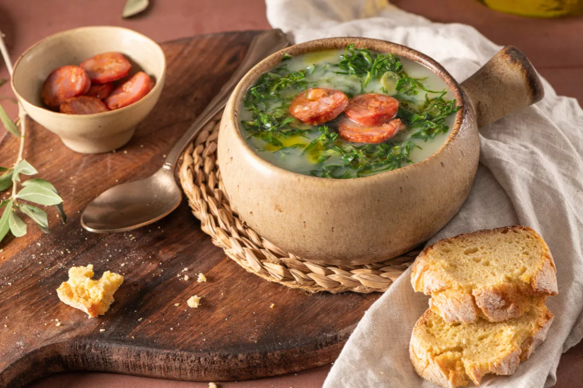 Tigela de caldo verde cremoso com couve e linguiça fatiada, acompanhada de pão caseiro, ideal para esquentar a noite do arraiá.