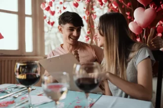 Casal sorridente sentado em restaurante decorado com corações vermelhos, analisando juntos um cardápio — clima romântico e descontraído para celebrar o Dia dos Namorados.
