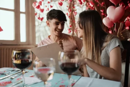 Casal sorridente sentado em restaurante decorado com corações vermelhos, analisando juntos um cardápio — clima romântico e descontraído para celebrar o Dia dos Namorados.