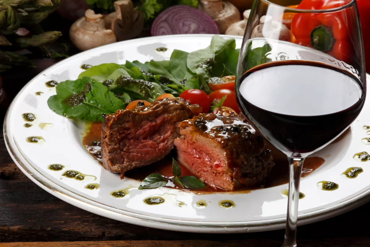 Medalhão de carne ao molho com ervas, acompanhado de salada verde e vinho tinto — prato principal sofisticado para cardápio fechado de restaurante no Dia dos Namorados.

