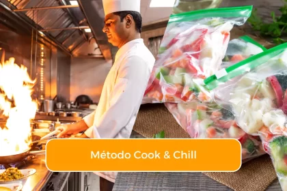 Chef profissional cozinhando em cozinha industrial com chama alta ao lado de alimentos preparados embalados a vácuo, representando o processo cook & chill em restaurantes.