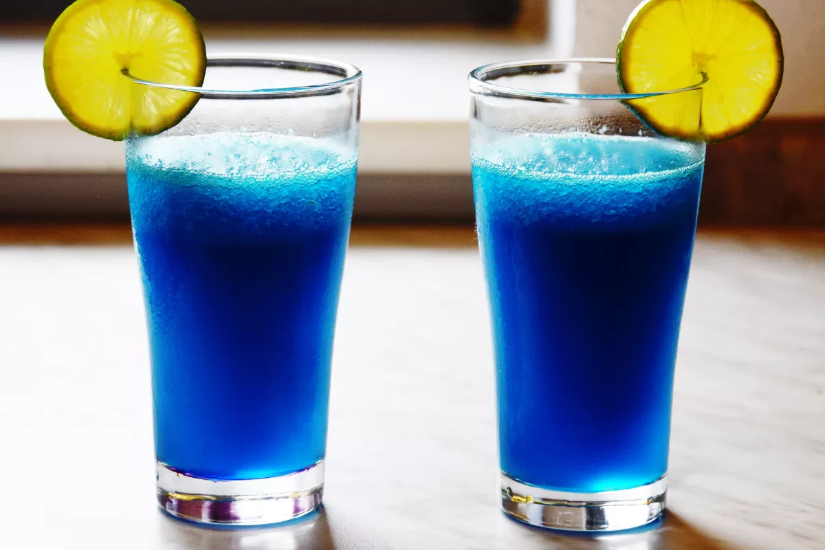 Dois copos altos com drink azul vibrante, decorados com rodelas de limão. Uma opção visualmente marcante para bares que apostam em coquetéis criativos.