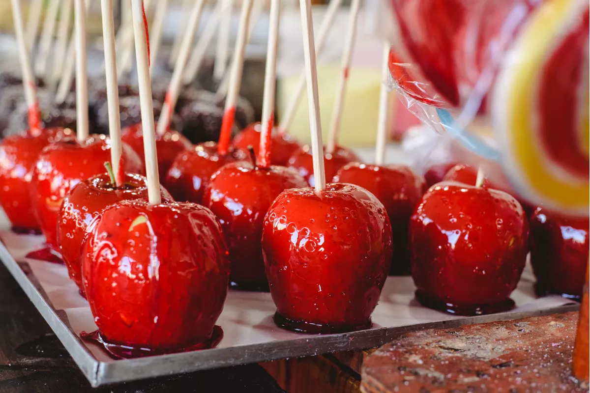 Maçãs do amor vermelhas, brilhantes e frescas, alinhadas em bandeja de festa junina, prontas para venda em barraquinhas típicas.