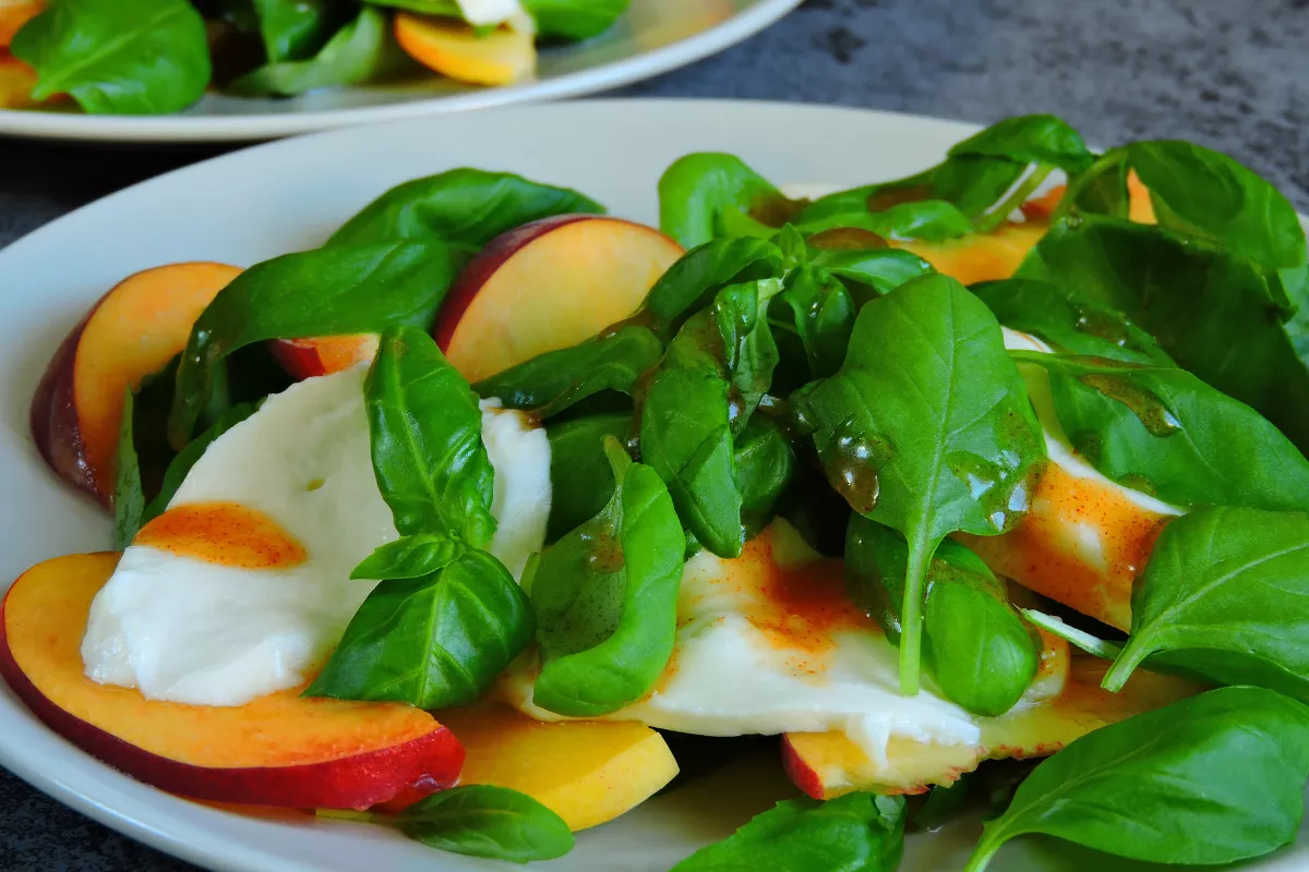 Prato com salada de folhas frescas, queijo branco e fatias de pêssego com molho balsâmico — opção leve e colorida para cardápio romântico saudável e vegano-friendly.