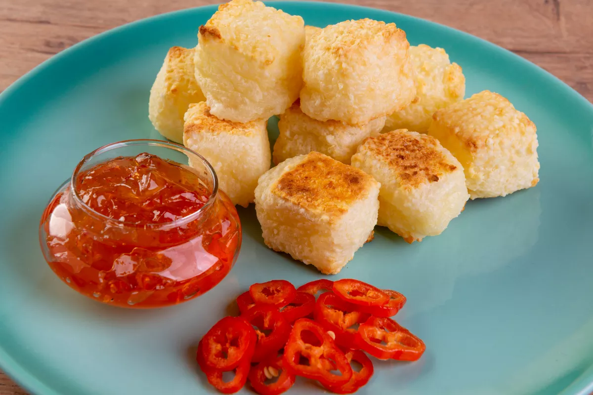 Cubos de queijo coalho dourados servidos com geleia de pimenta e fatias de pimenta vermelha fresca — petisco típico e prático para cardápios com mini porções e estilo finger food.


