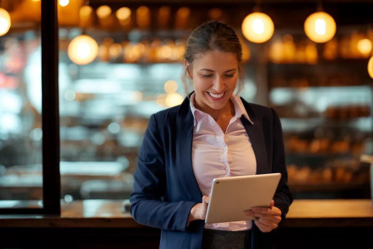 Gerente de restaurante sorrindo enquanto analisa dados em um tablet, representando o uso de tecnologia para conhecer melhor o perfil dos clientes.